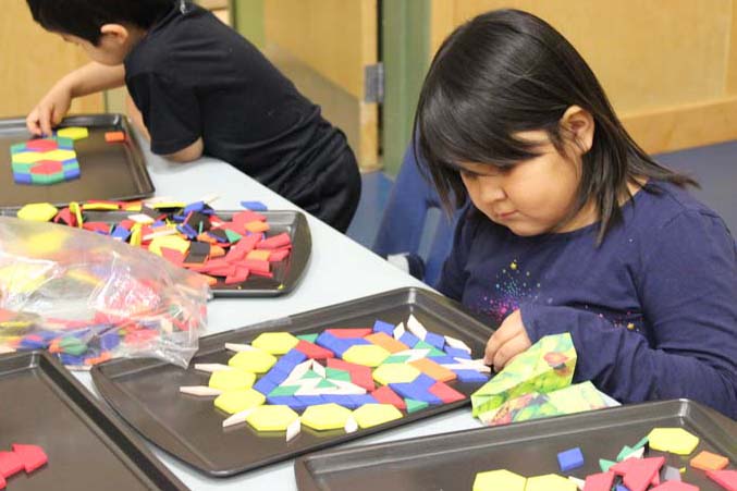 Student playing with magnetic pattern blocks on a cookie sheet