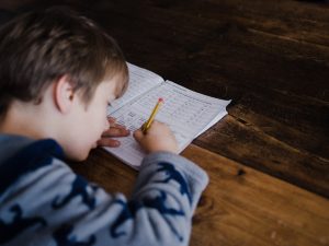 A primary-aged boy completes math problems in a workbook